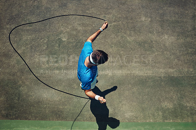 Buy stock photo High angle shot of a focused young man using a skipping rope as exercise outside on a tennis court during the day
