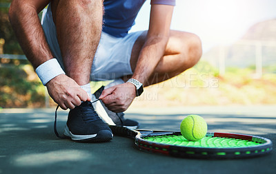 Buy stock photo Cropped shot of an unrecognizable male tennis player tying his shoelaces outdoors on a tennis court
