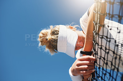 Buy stock photo Cropped shot of a young female tennis player feeling tired and slouching over the net on a tennis court outdoors