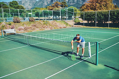 Buy stock photo Full length shot of a young male tennis player slouching over the net on a tennis court outdoors