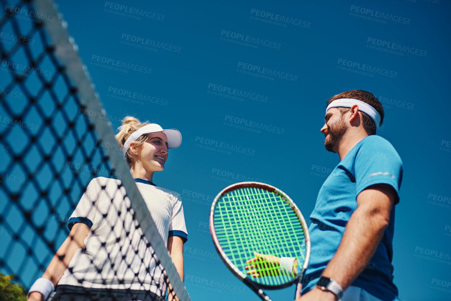 Buy stock photo Low angle shot of two young tennis players having a chat together outdoors on the court