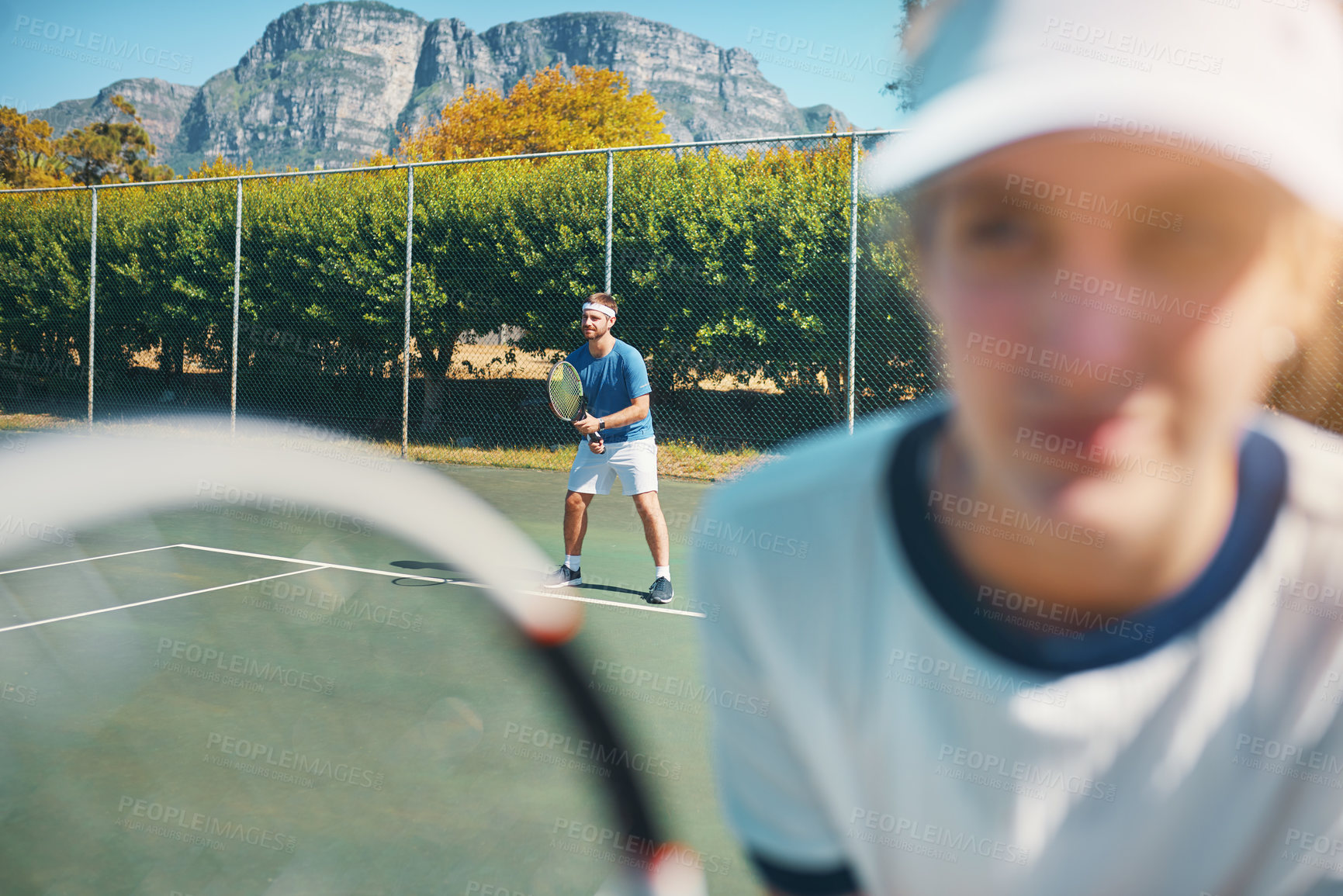 Buy stock photo Shot of a handsome young male tennis player outdoors on the court with a female teammate in the foreground