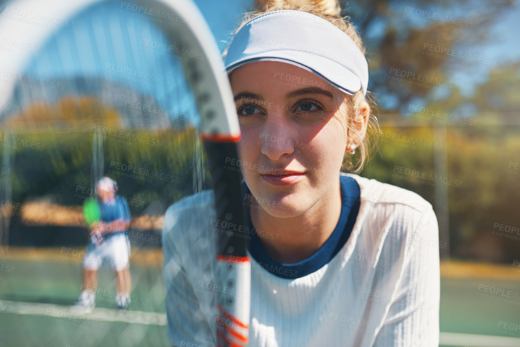 Buy stock photo Cropped shot of an attractive young female tennis player outdoors on the court with her male teammate in the background