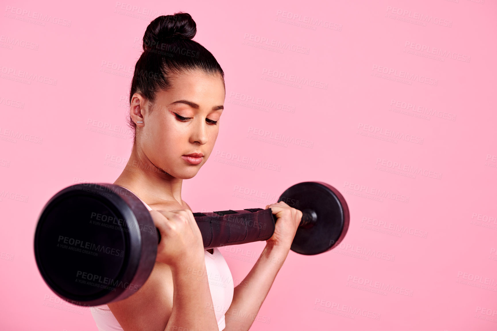 Buy stock photo Studio shot of a sporty young woman exercising with a barbell against a pink background
