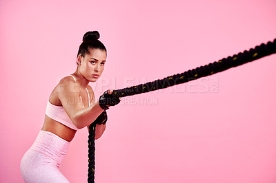 Buy stock photo Studio shot of a sporty young woman exercising with a battle rope against a pink background