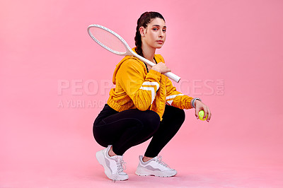 Buy stock photo Studio portrait of a sporty young woman posing with a tennis racket and ball against a pink background
