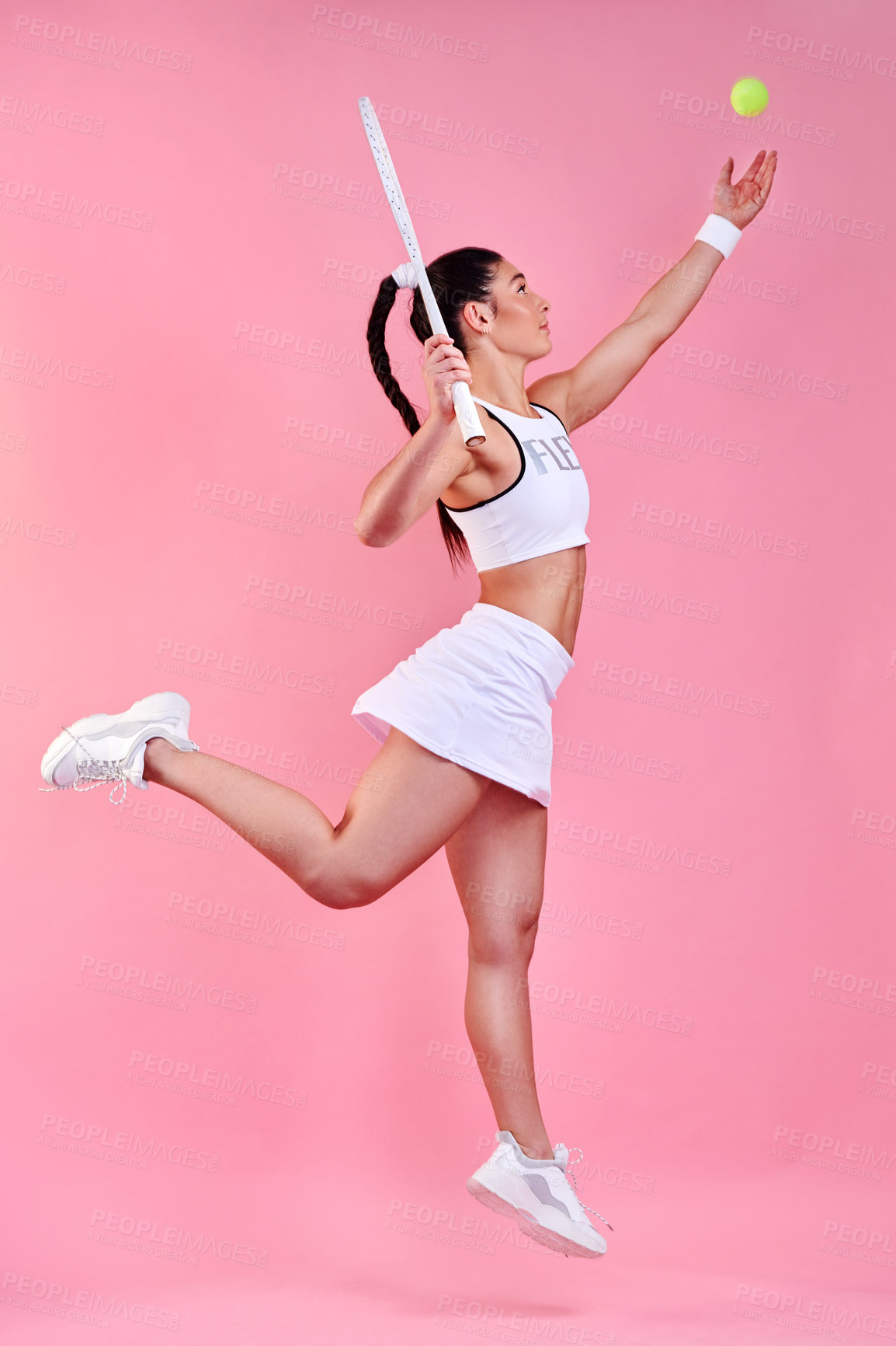 Buy stock photo Studio shot of a sporty young woman holding a tennis racket while throwing a tennis ball against a pink background