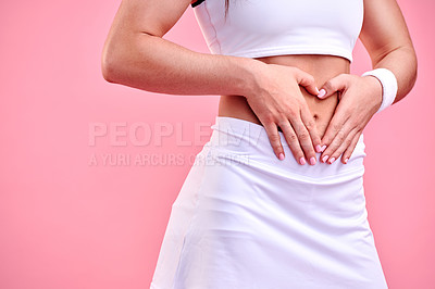 Buy stock photo Studio shot of a sporty woman making a heart shape with her hands over her stomach against a pink background