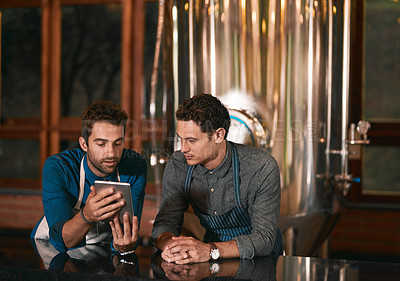 Buy stock photo Shot of two businessmen browsing on a cellphone together inside of a beer brewery during the day