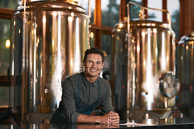 Buy stock photo Portrait of a cheerful young businessman seated at a table inside of a beer brewery  during the day