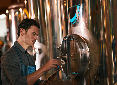 Buy stock photo Shot of a young working man doing inspection of their beer making machinery inside of a beer brewery during the day