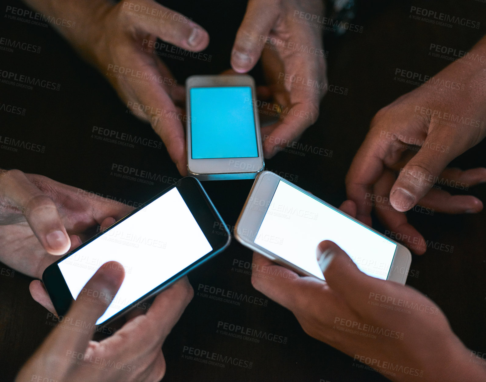 Buy stock photo High angle shot of three unrecognizable people seated in a circle at a table while browsing on their cellphones