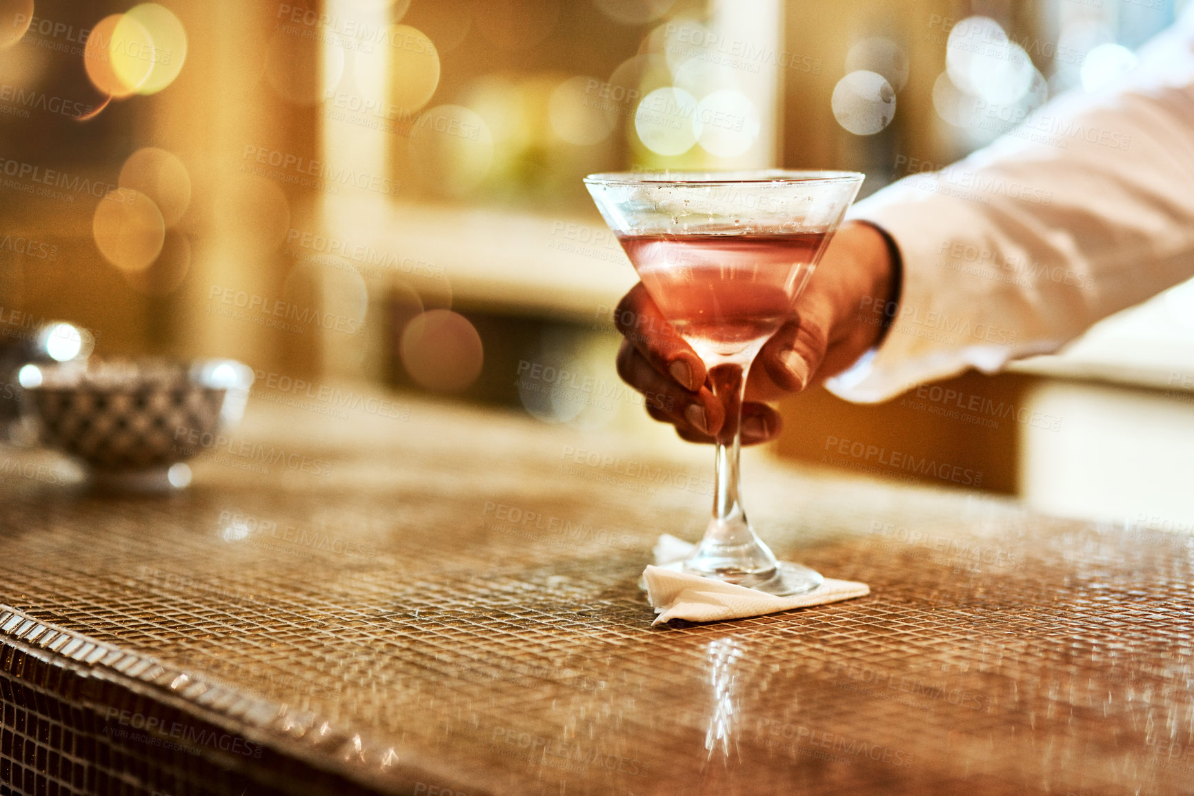 Buy stock photo Cropped shot of an unrecognizable barman serving a drink on the bar counter inside of an establishment at night