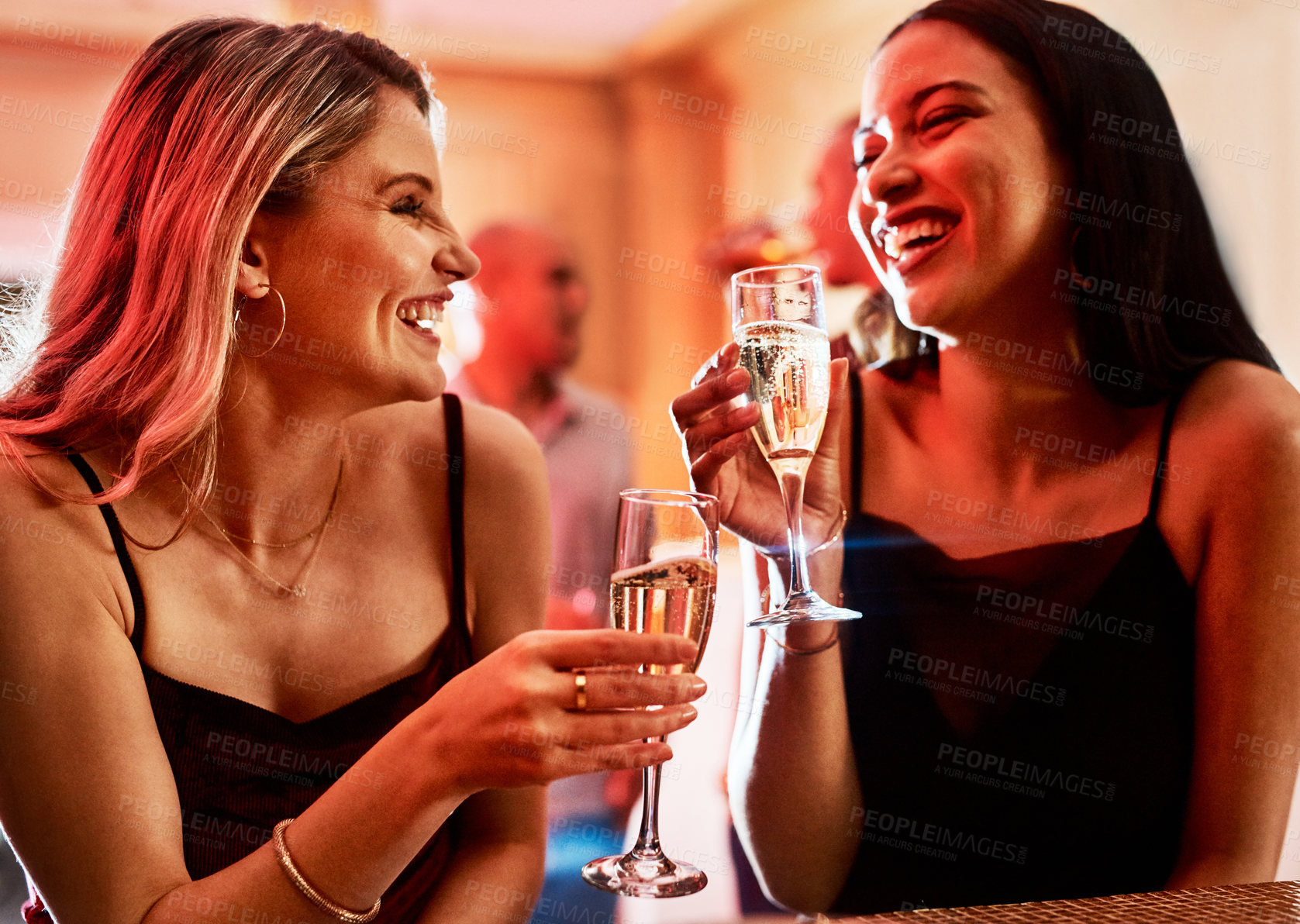Buy stock photo Cropped shot of two cheerful young women chatting while having drinks inside of a bar at night