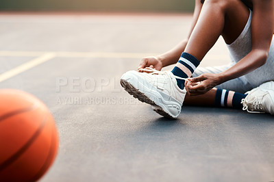 Buy stock photo Cropped shot of an unrecognizable sportswoman sitting on the court and tying her shoelaces before playing a game of basketball