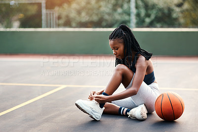Buy stock photo Cropped shot of an attractive young sportswoman sitting on the court and tying her shoelaces before playing basketball