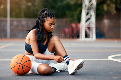 Buy stock photo Cropped shot of an attractive young sportswoman sitting on the court and tying her shoelaces before playing basketball