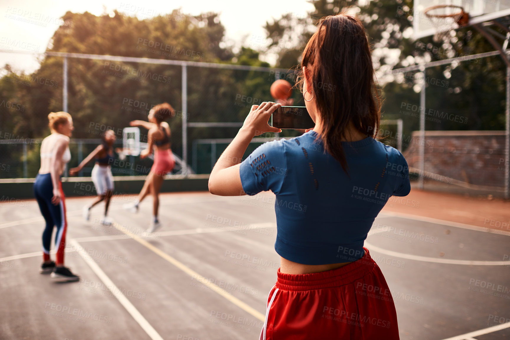 Buy stock photo Cropped shot of an unrecognizable sportswoman standing and filming her team with a cellphone during a basketball game