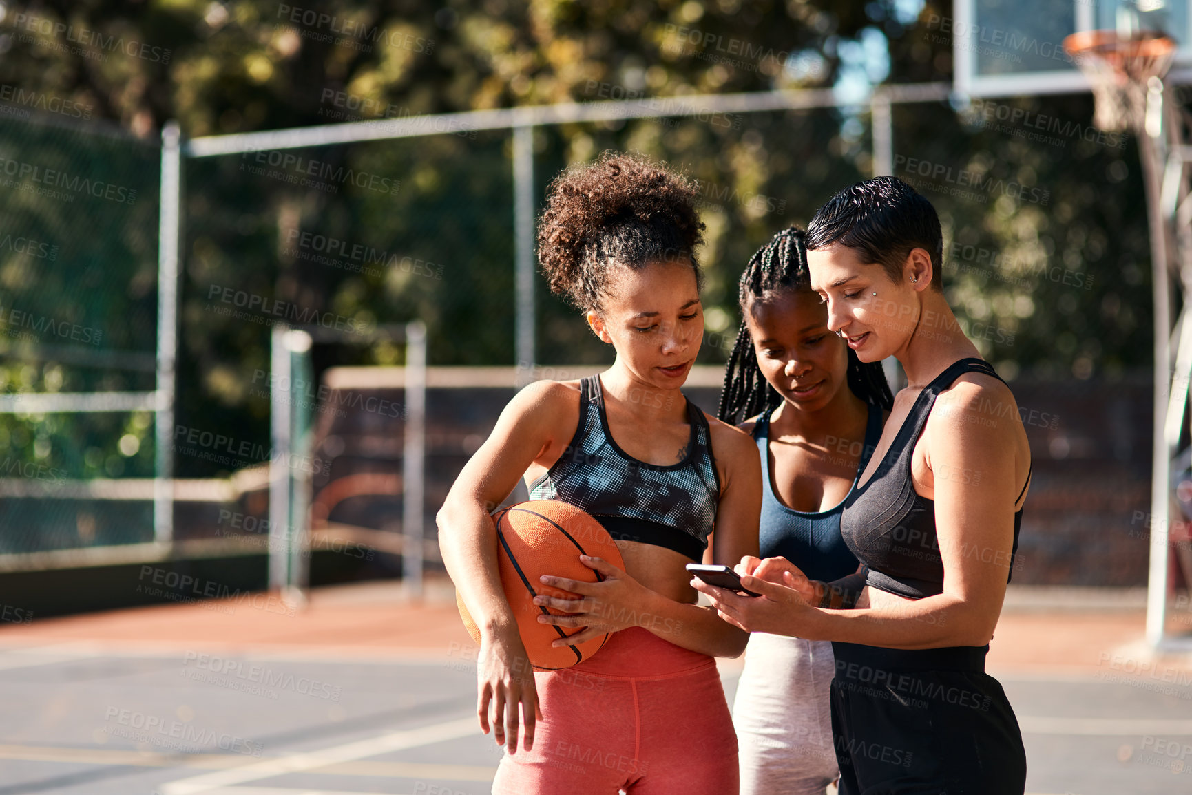 Buy stock photo Cropped shot of a diverse group of sportswomen standing together after playing basketball and looking at a cellphone