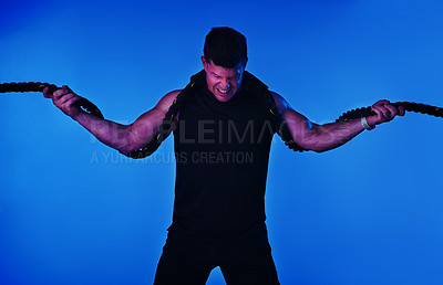 Buy stock photo Blue filtered shot of a man working out with battle ropes in the studio
