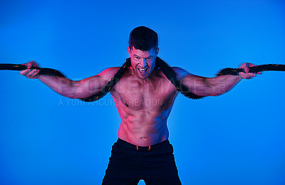 Buy stock photo Blue filtered shot of a man working out with battle ropes in the studio