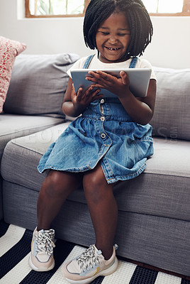 Buy stock photo Full length shot of an adorable little girl using a digital tablet while sitting on a sofa at home