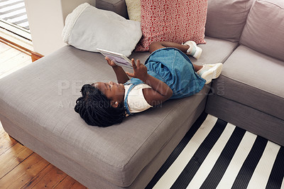 Buy stock photo Full length shot of an adorable little girl using a digital tablet while lying down on a sofa at home