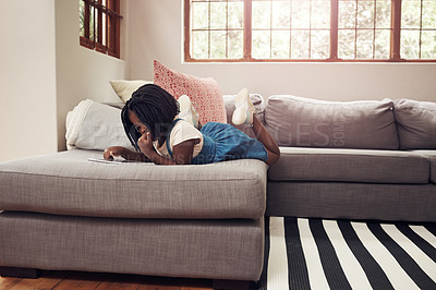 Buy stock photo Full length shot of an adorable little girl using a digital tablet while lying down on a sofa at home
