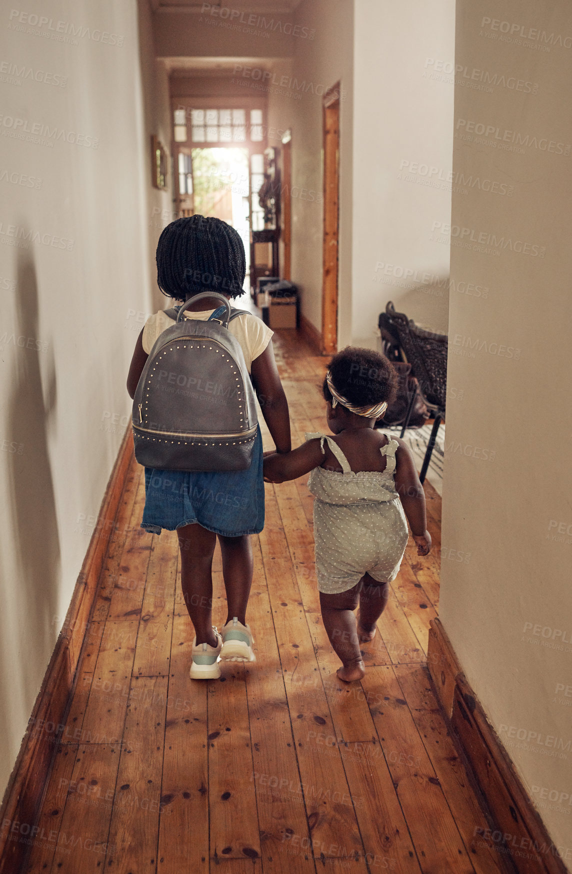 Buy stock photo Rearview shot of a young school girl walking with her baby sister through the passage at home