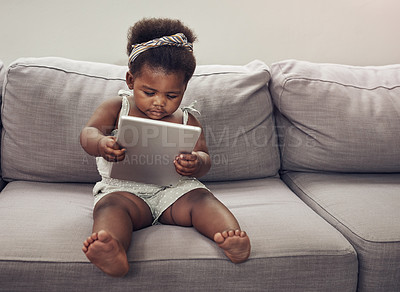 Buy stock photo Full length shot of an adorable baby girl using a digital tablet while sitting on a sofa at home