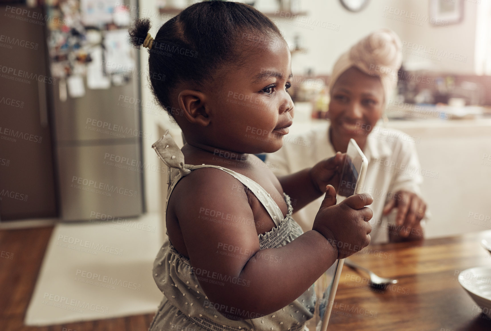Buy stock photo Cropped shot of an adorable baby girl eating breakfast in the kitchen with her mother in the background