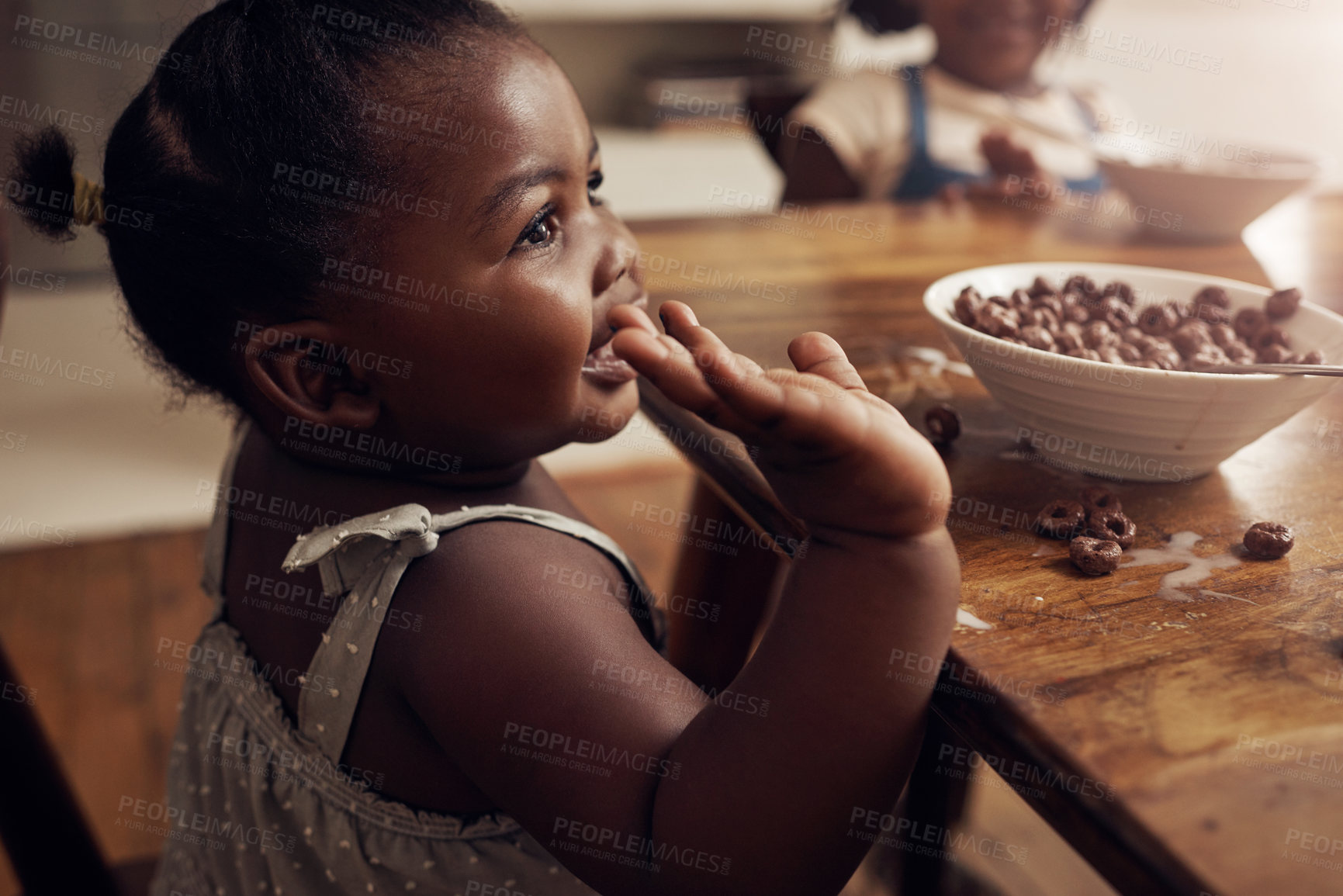 Buy stock photo Cropped shot of an adorable baby girl eating cereal at home with her elder sister in the background
