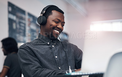 Buy stock photo Cropped shot of a handsome young businessman using a laptop while wearing headphones in a modern office