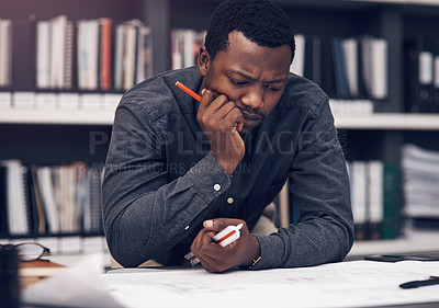 Buy stock photo Cropped shot of a handsome young male architect looking thoughtful while working with blueprints in a modern office