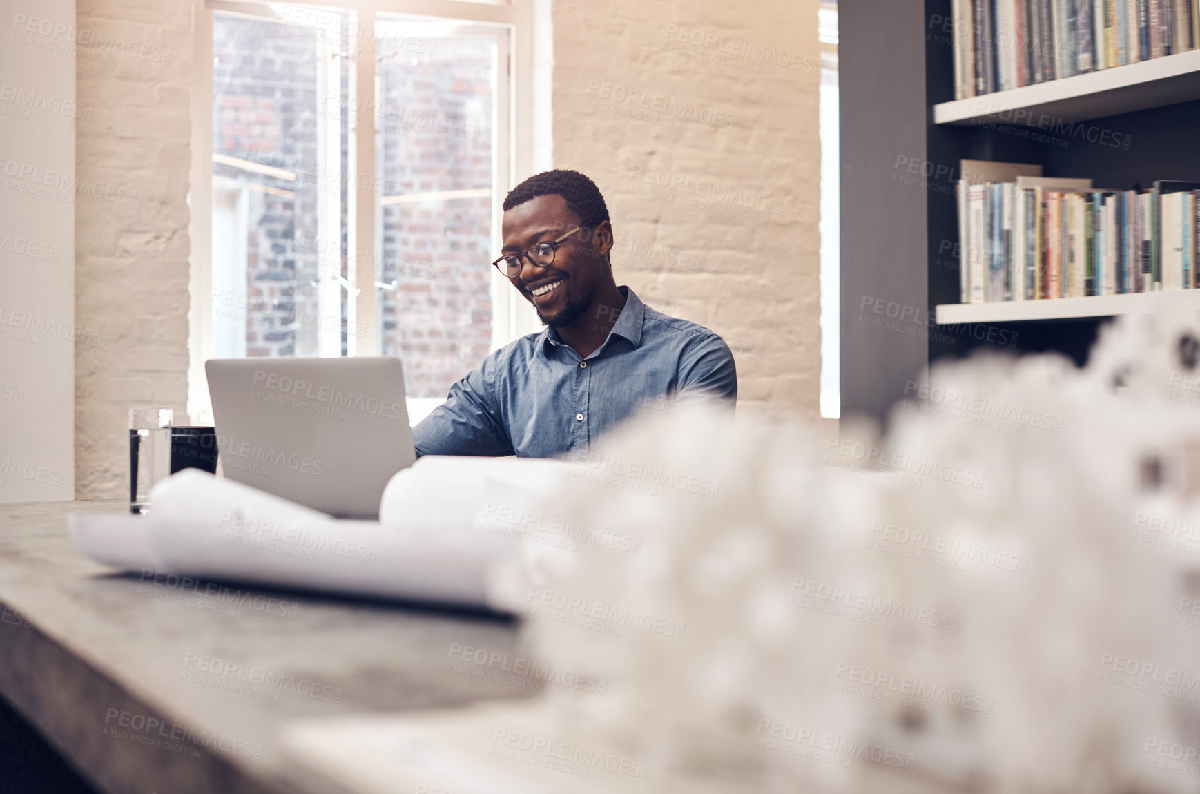Buy stock photo Cropped shot of a handsome young male architect smiling while working on a laptop in a modern office