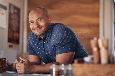 Buy stock photo Portrait of a cheerful young coffee barista leaning on the counter of his coffee truck to serve customers outside during the day