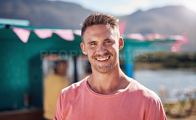 Buy stock photo Portrait of a cheerful young man smiling brightly while standing outside on a beach promenade during the day