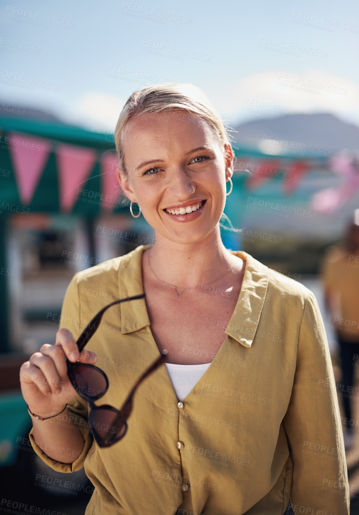 Buy stock photo Portrait of a cheerful young woman smiling brightly while standing outside on a beach promenade during the day