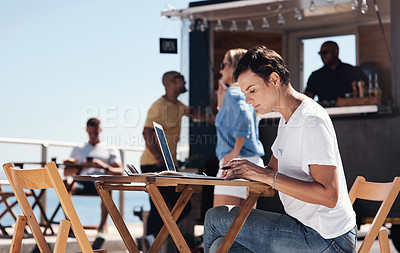 Buy stock photo Cropped shot of a focused young woman working on her laptop while being seated at a table next to a beach promenade outside during the day