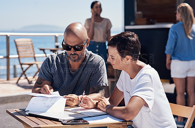 Buy stock photo Cropped shot of two confident young businesspeople having a meeting together while making use of a digital tablet outside next to a beach promenade