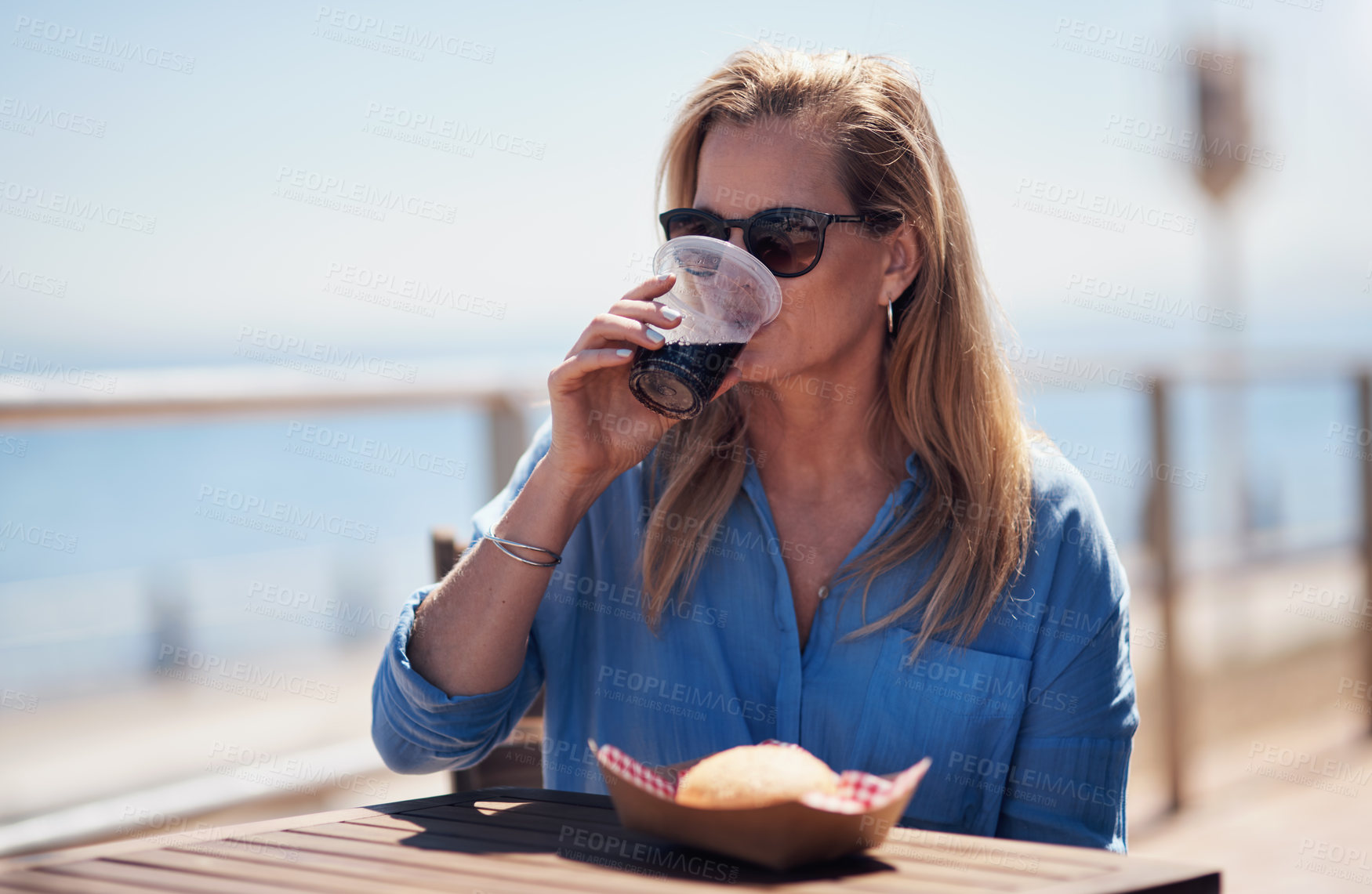 Buy stock photo Cropped shot of a carefree middle aged woman having lunch outside next to a beach promenade during the day