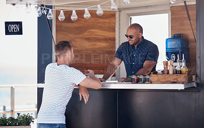 Buy stock photo Cropped shot of two cheerful young work colleagues having a chat next to their coffee truck outside during the day