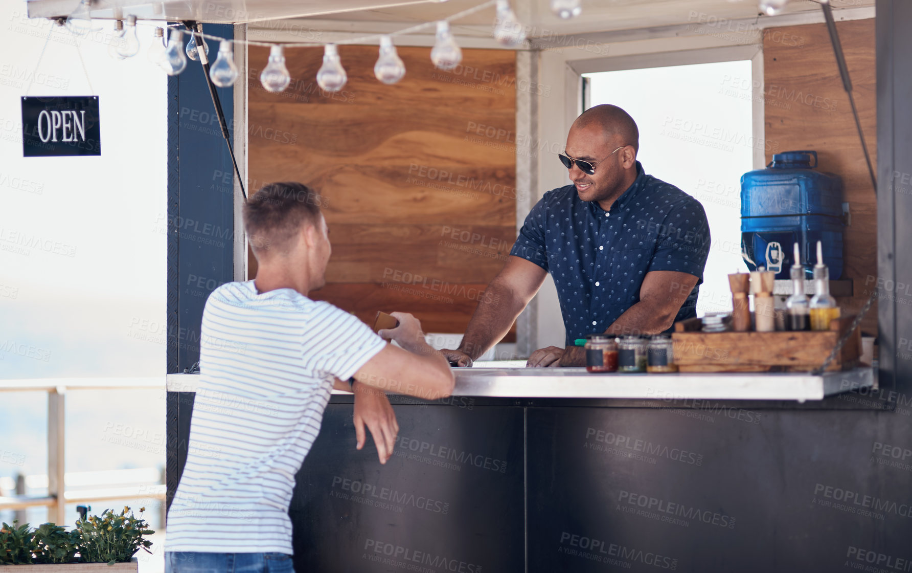 Buy stock photo Cropped shot of two cheerful young work colleagues having a chat next to their coffee truck outside during the day