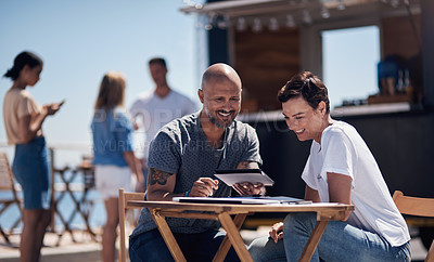 Buy stock photo Cropped shot of two confident young businesspeople having a meeting together while making use of a digital tablet outside next to a beach promenade