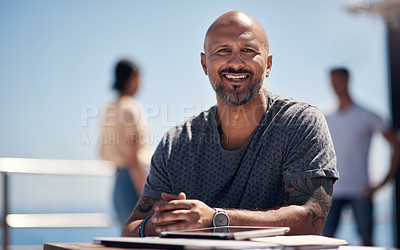 Buy stock photo Portrait of a cheerful middle aged man seated at a table outside next a beach promenade