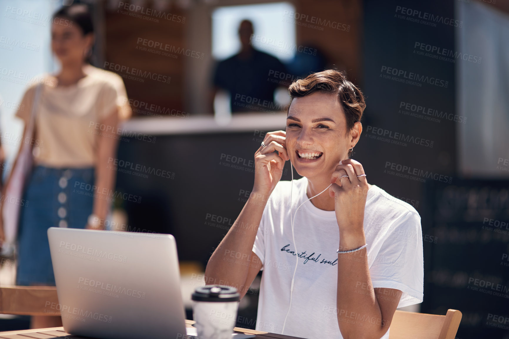 Buy stock photo Portrait of a cheerful young woman listening to music while working on her laptop next to a coffee truck outside during the day