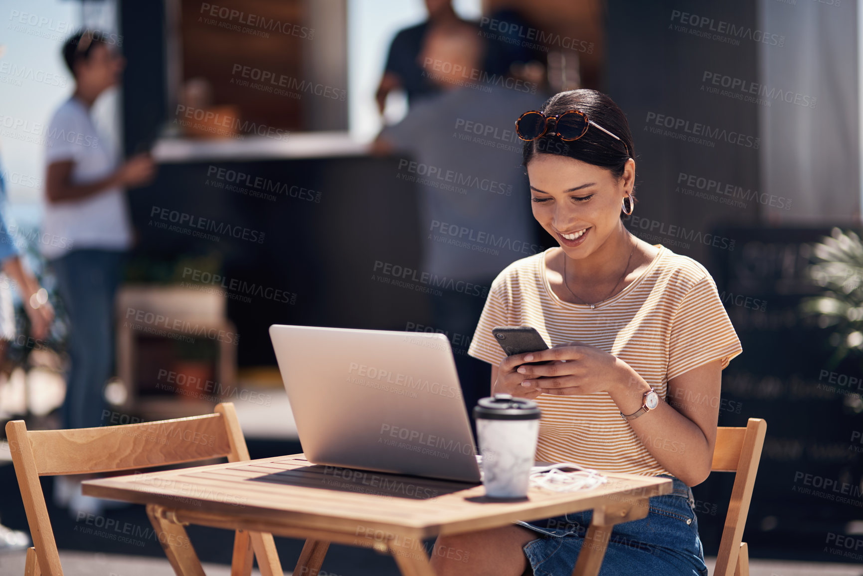 Buy stock photo Cropped shot of a cheerful young woman texting on her cellphone while doing work on her laptop next to a beach promenade outside during the day