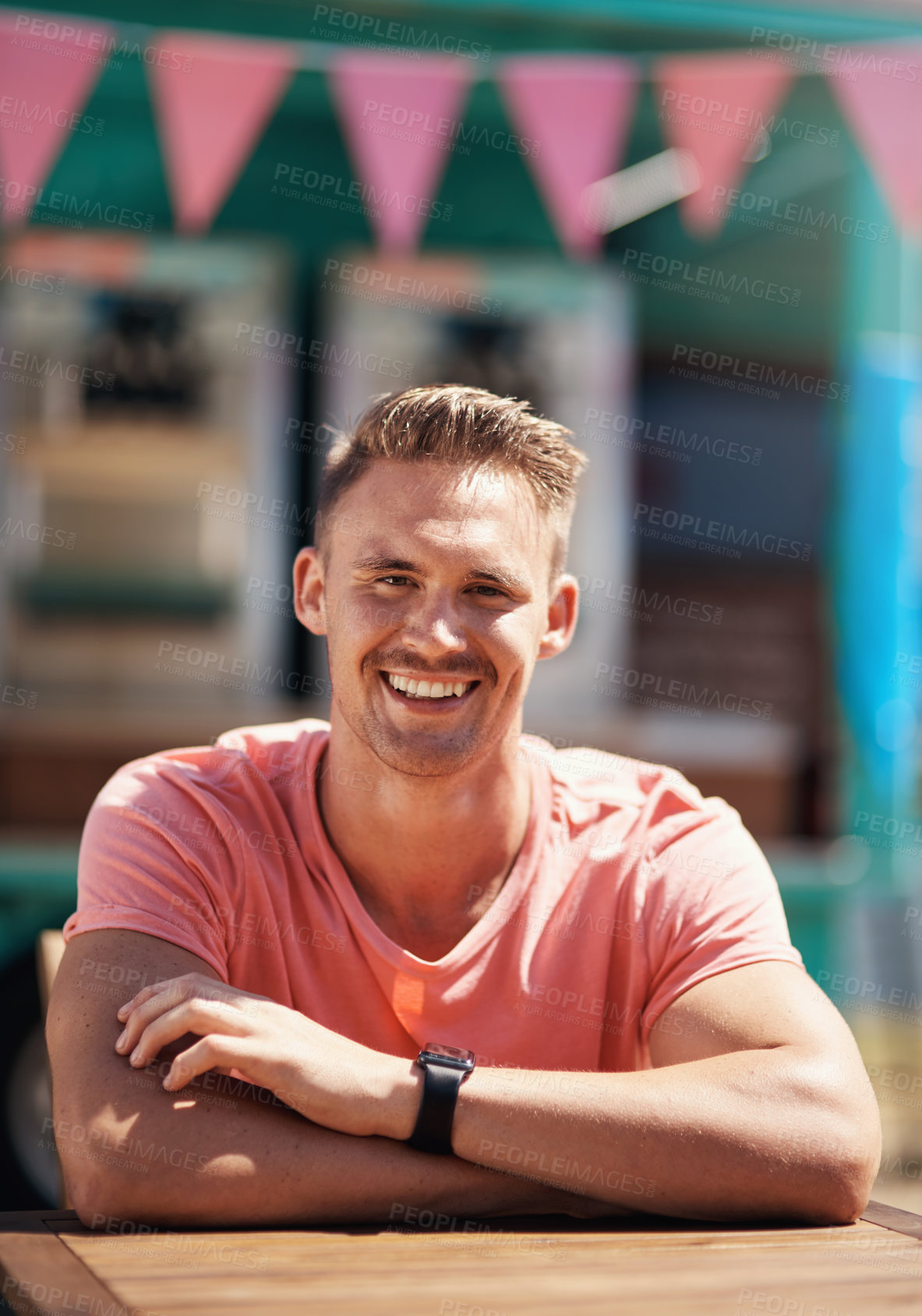 Buy stock photo Portrait of a cheerful man seated at a table by himself outside next to a beach promenade during the day