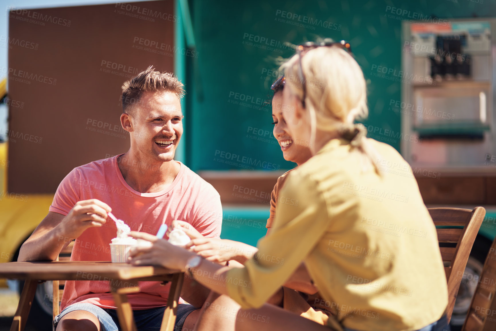 Buy stock photo Cropped shot of a group of cheerful young friends having lunch together outside next to a beach promenade
