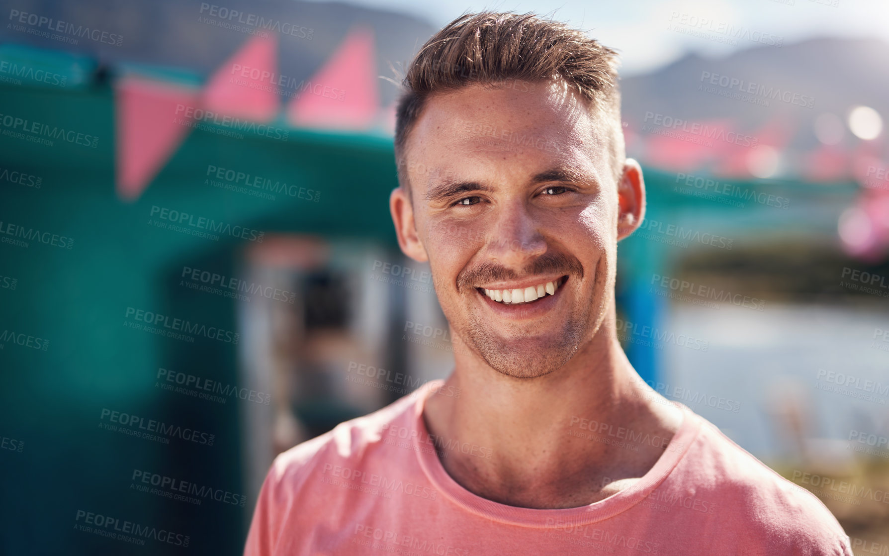 Buy stock photo Portrait of a cheerful young man smiling brightly while standing outside on a beach promenade during the day